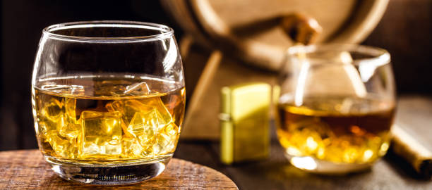 istock whiskey glass with ice, spot focus, bottle, lighter and barrel on blurred background. Distilled drink with malt 1300336813