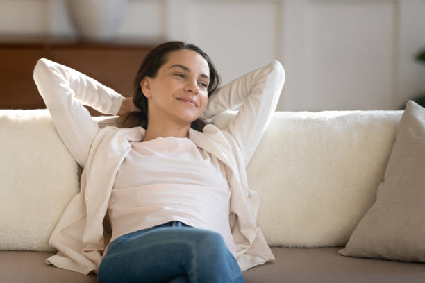 istock Successful woman resting on sofa looking aside with dreamy smile 1300340804
