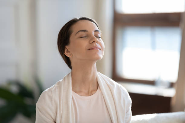 Content woman sitting on sofa with closed eyes breathing air Calm leisure. Content young woman spending time at home alone, sitting on sofa with eyes closed in delight, breathing fresh cool air because of working conditioner, giving face to sunlight from window wind stock pictures, royalty-free photos & images