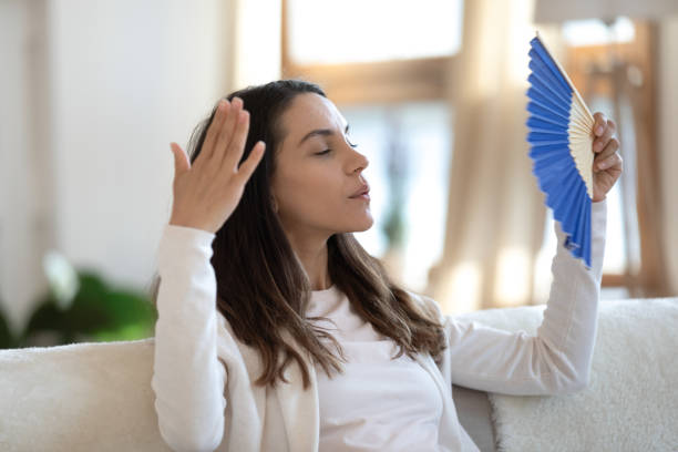 istock Stressed female sitting on couch waving herself with hand fan 1300340961