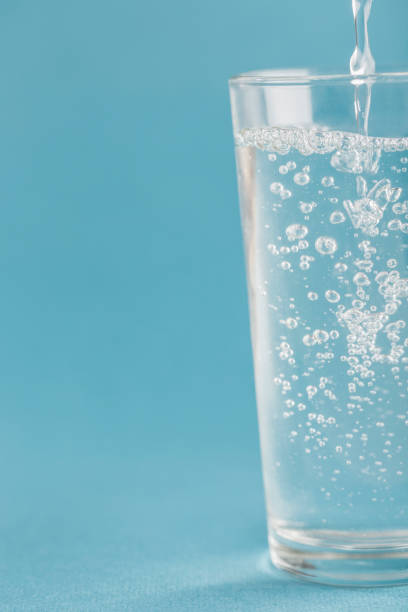 istock Clean water is poured into a glass on a blue background close-up. 1300342893