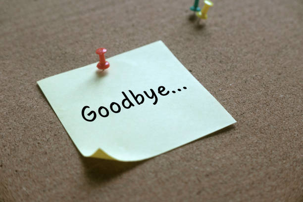 Selective focus of colorful push pins and yellow memo notes written with Goodbye... on a cork board.