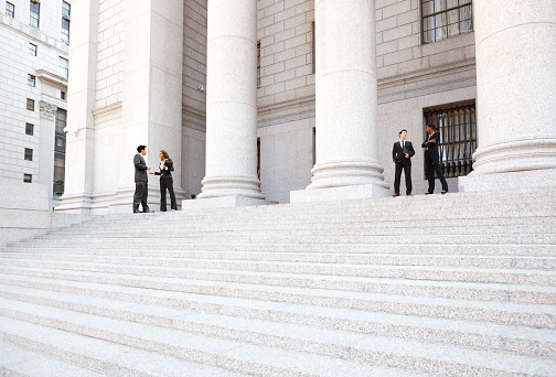 Four well dressed professionals in discussion on the exterior steps of a courthouse. Could be lawyers, business people etc.