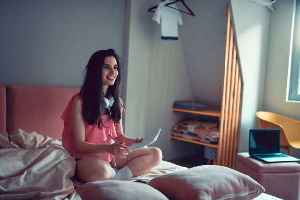 istock Smiling Female Student Enjoying Music While Writing School Paper In Campus Dorm 1300344365