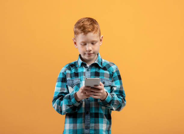 istock Cute ginger kid with mobile phone on yellow 1300346074