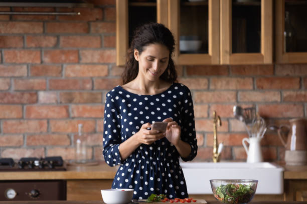 istock Smiling woman cooking food using cellphone in kitchen 1300347639
