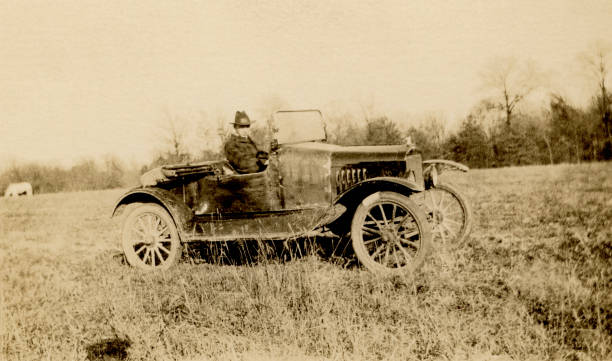 teenage boy learning to drive a car in 1918 Young man learning to drive a circa 1915 roadster car in a farm field in 1918. 1918 stock pictures, royalty-free photos & images
