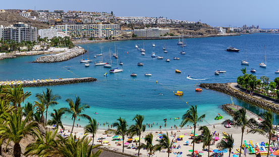 Summer landscape with a beach with people bathing, hotels and boats anchored in the sea. Gran Canaria. Arguineguin.