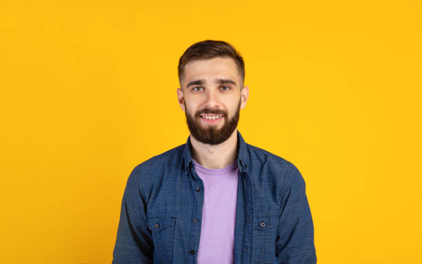 istock Carefree young guy looking at camera and smiling over orange studio background, panorama 1300351401
