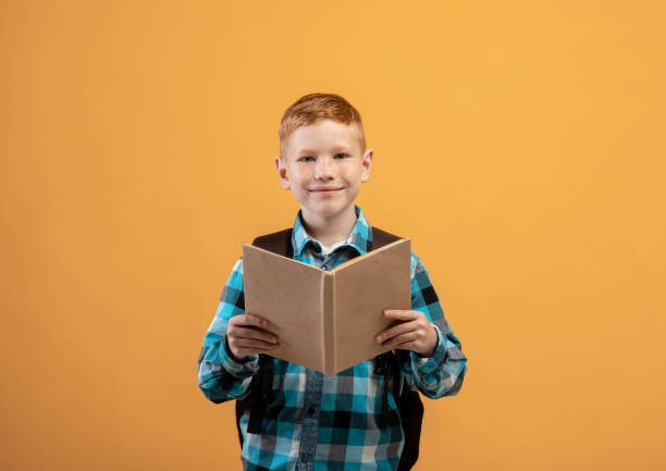 istock Cute ginger kid schooler reading book, yellow studio background 1300351677