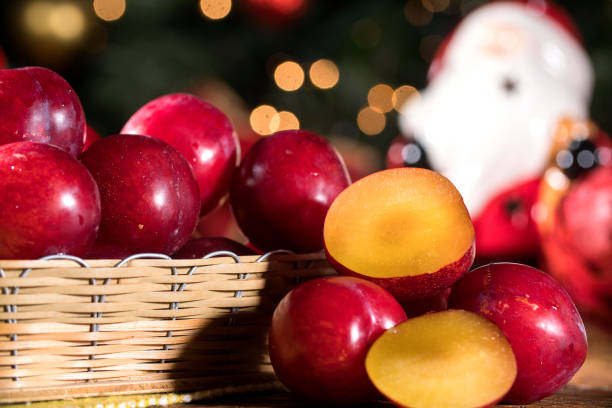 袋布とぼやけたクリスマスの背景を持つ木製のテーブルの上の籐のバスケットに梅 - plum fruit basket wicker ストックフォトと画像