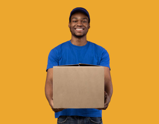 istock Black delivery man holding cardboard box showing it to camera 1300352604