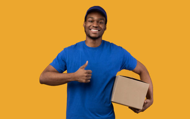 istock Black delivery man holding cardboard box showing thumb up 1300352761