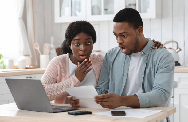 Shocked black couple in kitchen having financial problems, doing family budget calculations Shocked black couple in kitchen stressed with financial problems, doing calculations of family budget together. Frustrated african american spouses sitting at table looking at loan documents receipt photos stock pictures, royalty-free photos & images
