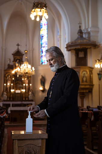 Priest in church disinfecting his hands