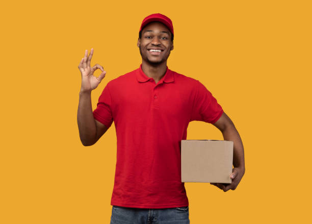 istock Black delivery man holding cardboard box showing okay sign 1300356533