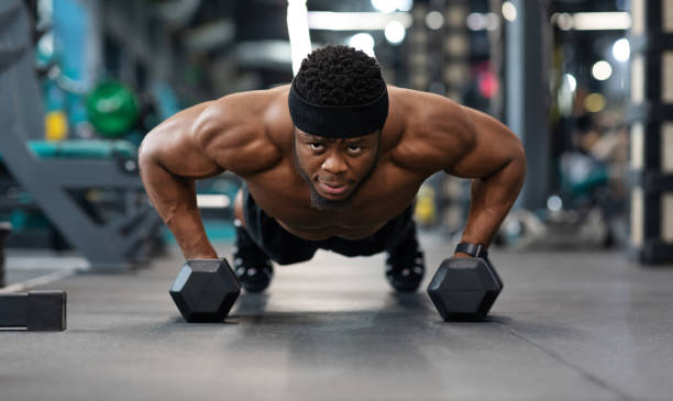 istock Confident black guy sportsman pushing up with dumbbells 1300357201