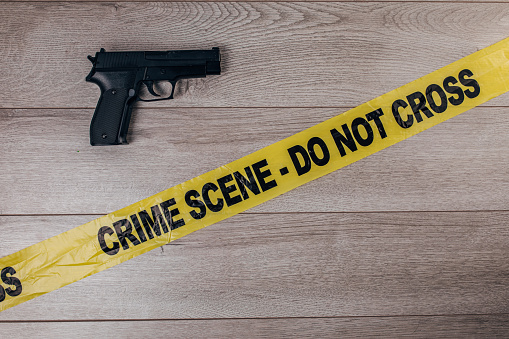 Yellow crime scene tape and gun on wooden background. Top view. Flat lay concept.