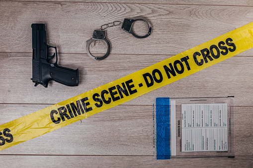 Yellow crime scene tape, handcuffs, evidence bag and gun on wooden background. Top view. Flat lay concept.