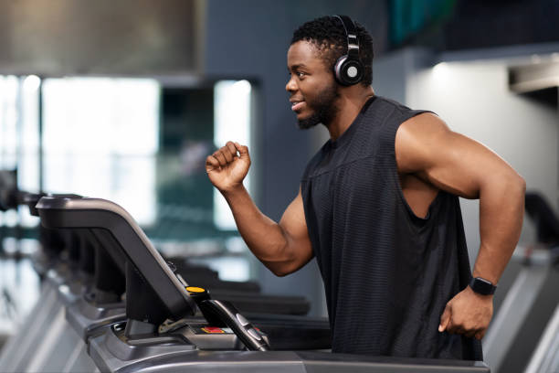 hombre negro alegre en auriculares inalámbricos modernos corriendo en el gimnasio - body building exercises audio fotografías e imágenes de stock