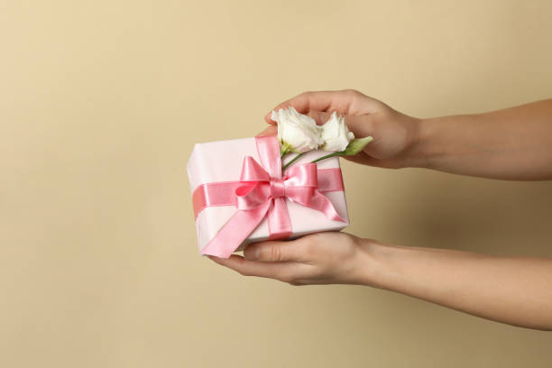 istock Female hands hold gift box with roses on beige background 1300358591