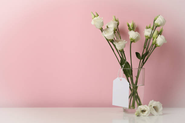 istock Vase with roses and blank tag against pink background 1300358711