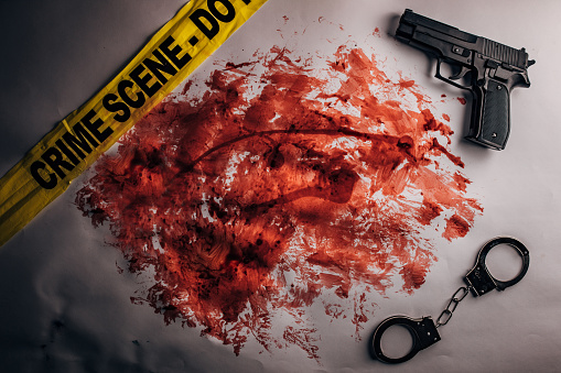 Yellow crime scene tape, handcuffs, gun and blood stain on white background. Top view. Flat lay concept.