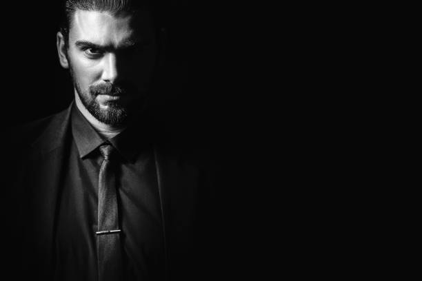 Business portrait of a white caucasian man in a black classic suit on a black background. Bearded man looks confident eyes. Business portrait of a white caucasian man in a black classic suit on a black background. Bearded man looks confident eyes. black and white men facial hair beard stock pictures, royalty-free photos & images