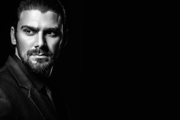 Black and white male portrait. A man in a black classic suit in a black shirt and tie over a black background. Dark-haired young man. Black and white male portrait. A man in a black classic suit in a black shirt and tie over a black background. Dark-haired young man. black and white men facial hair beard stock pictures, royalty-free photos & images