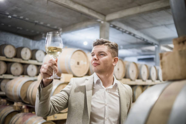 sommelier wine tasting. the owner of the winery checks the quality and stocks of wine in the wine cellar, around it are wooden barrels with quality wine. regular inspection of the wine cellar and wine tasting. - half tank imagens e fotografias de stock