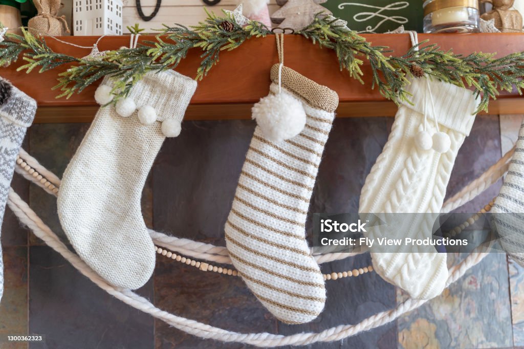 Hygge lifestyle at home during Christmas Close up of white Christmas stockings and winter holiday decorations in modern farmhouse Scandinavian design above fireplace in cozy family living room. Christmas Stocking Stock Photo