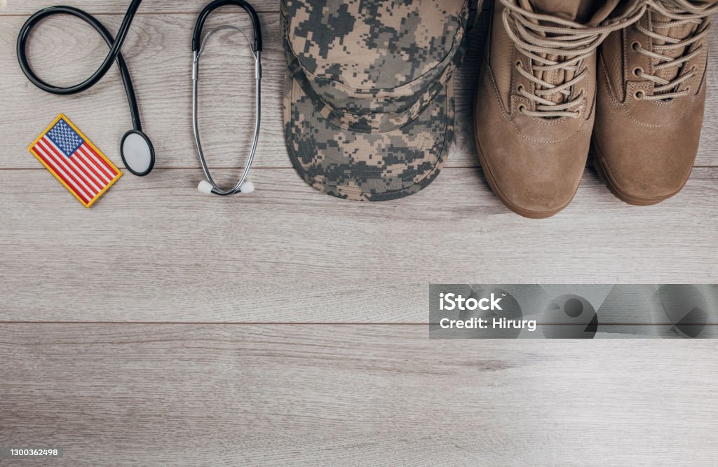 US military doctor equipment Top view of camouflaged military cap, stethoscope, US flag and boots on wooden background. Flat lay concept. American Flag Stock Photo