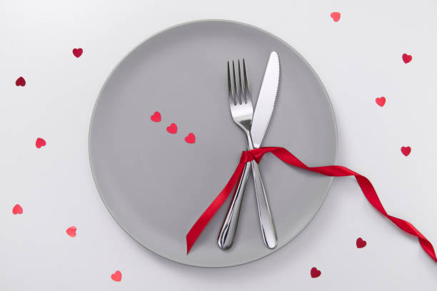 istock Valentine's day festive table setting, flat lay with red heart shape on gray plate, fork, knife and red ribbons on white table. Love dating concept. Place your text and copy space 1300362802