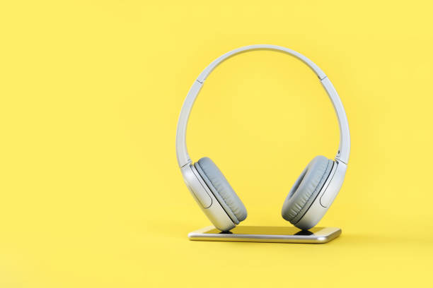 istock Wireless gray headphones with mobile on illuminating yellow background 1300364229