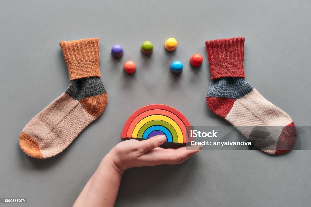 Odd Socks Day. Mismatched socks, hand holding wooden rainbow, toy figures. Social initiative against bullying in school or workplace. Design for anti-bullying campaign poster or cards Odd Socks Day.Mismatched socks, hand hold wooden rainbow, toy figures. Social initiative against bullying in school or workplace. Design for anti-bullying campaign visual. Above Stock Photo