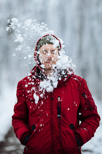 Young man getting hit by a snowball while walking in a forest