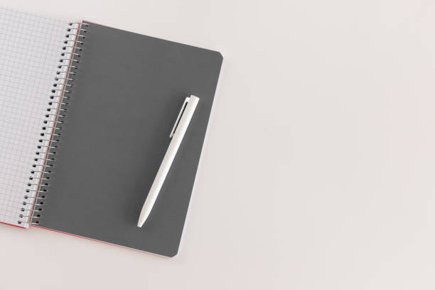 istock Spiral opened notebook with gray sheet and white pen. Layout and flat lay with place for text isolated on white background. Back to school. Top view, copy space. High resolution. Student workplace 1300368080