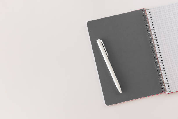 istock Spiral opened notebook with gray sheet and white pen. Layout and flat lay with place for text isolated on white background. Back to school. Top view, copy space. High resolution. Student workplace 1300368081