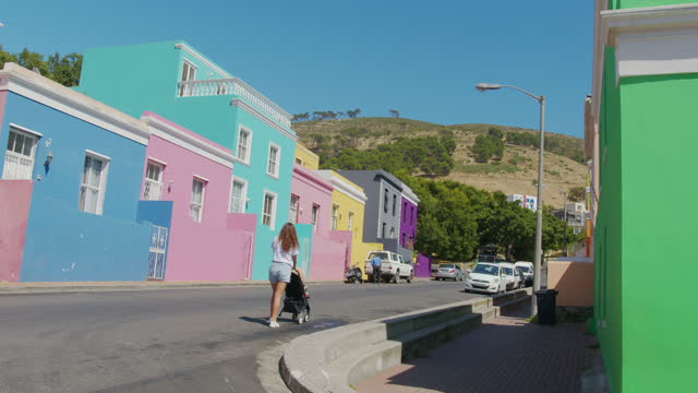 Woman walking with baby stroller in the streets of colorful buildings neighbourhood Bo-Kaap Cape Town South Africa.