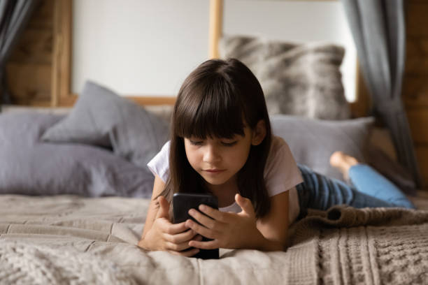 istock Close up curious little girl using phone, lying on bed 1300371813