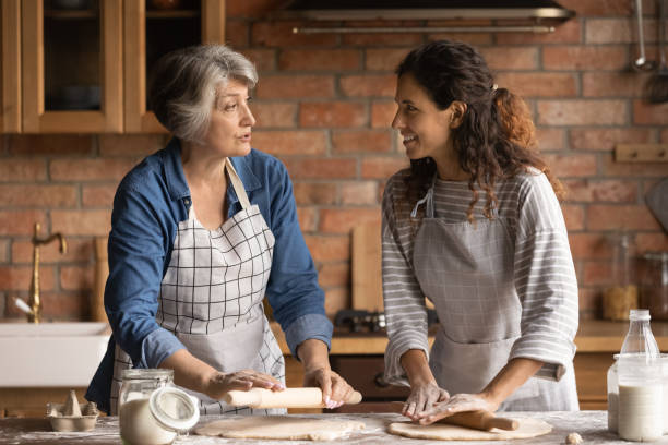 reife frau mit erwachsenen tochter plaudern, kochen hausgemachte gebäck - grandmother cooking baking family stock-fotos und bilder