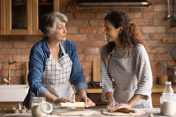 mature woman with grownup daughter chatting, cooking homemade pastry - grandmother cooking baking family imagens e fotografias de stock