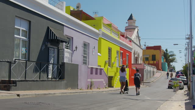 Woman walking with son and baby stroller in the streets of colorful buildings neighbourhood Bo-Kaap Cape Town South Africa.