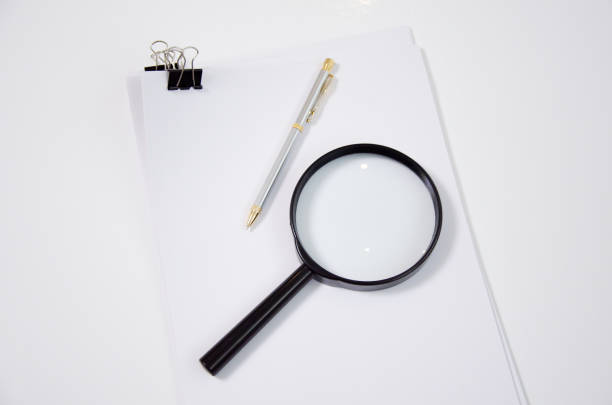 istock A4 paper, pen and reading glass, magnifying glass, isolated white in studio. 1300378420