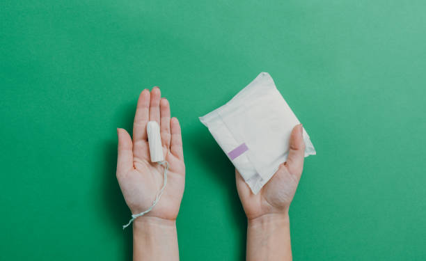 mãos femininas segurando copo menstrual e almofada sanitária sobre fundo verde - tampon healthcare and medicine menstruation indoors - fotografias e filmes do acervo