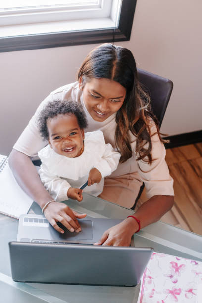 razza mista madre indiana con bambino nero africano che lavora online da casa su internet. posto di lavoro di donna freelance con bambino. resta a casa mamma single che lavora a distanza. una nuova normalità. - multi tasking asian and indian ethnicities asian ethnicity lifestyles foto e immagini stock