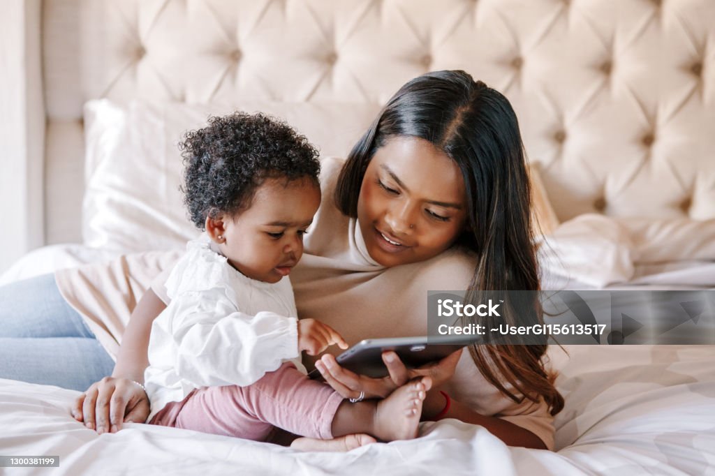 Mixed race Indian black mother with toddler baby girl watching cartoons on a tablet. Ethnic diversity. Family mom with kid using technology. Video chat, video call. Black people community. Mixed race Indian black mother with toddler baby girl watching cartoons on tablet. Ethnic diversity. Family mom with kid using technology. Video chat, video call. Black people community. Baby - Human Age Stock Photo