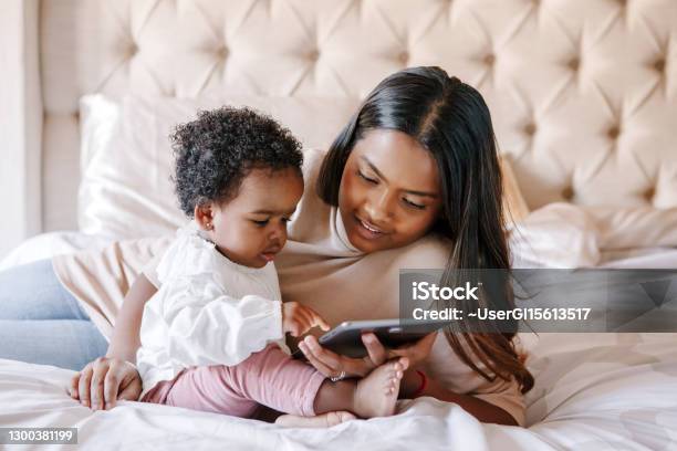 Mixed Race Indian Black Mother With Toddler Baby Girl Watching Cartoons On A Tablet Ethnic Diversity Family Mom With Kid Using Technology Video Chat Video Call Black People Community Stock Photo - Download Image Now