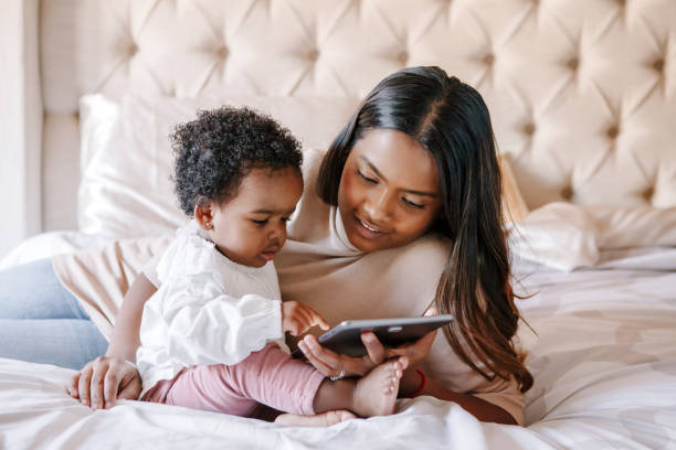 mixed race indian black mother with toddler baby girl watching cartoons on a tablet. ethnic diversity. family mom with kid using technology. video chat, video call. black people community. - family african ethnicity black african descent imagens e fotografias de stock