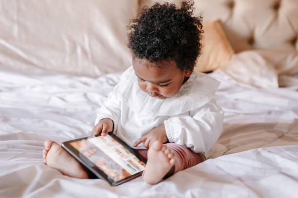 Mixed race African black toddler baby girl watching cartoons on tablet. Ethnic diversity. Little kid child using technology. Early age education development. Video chat or video call. Mixed race African black toddler baby girl watching cartoons on tablet. Ethnic diversity. Little kid child using technology. Early age education development. Video chat, video call. screen time and technology in babies stock pictures, royalty-free photos & images